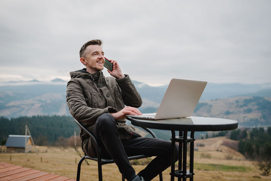 Freelancer out in nature working on his laptop whilst answering a phone call